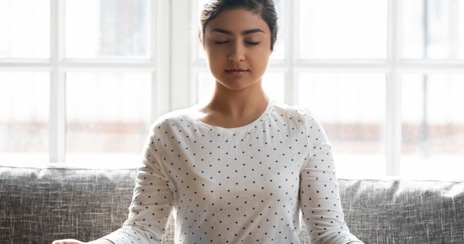 Calm Indian Woman With Closed Eyes Meditating Home Alone Close Up Relaxed Beautiful Girl Sitting Lotus Pose Comfortable Couch Dreaming Doing Yoga Exercise Stress Relief Concept