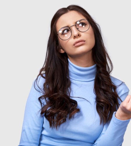 Portrait Of Serious Young Businesswoman Wearing Blue Long Sleeve Blouse And Round Transparent Eyeglasses. European Female Office Worker Thinking And Looking At One Side On White Studio Wall.